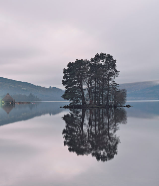 A classic view down the length of Loch Tay, hints of mist in the distant mountains and trees on the foreground island.